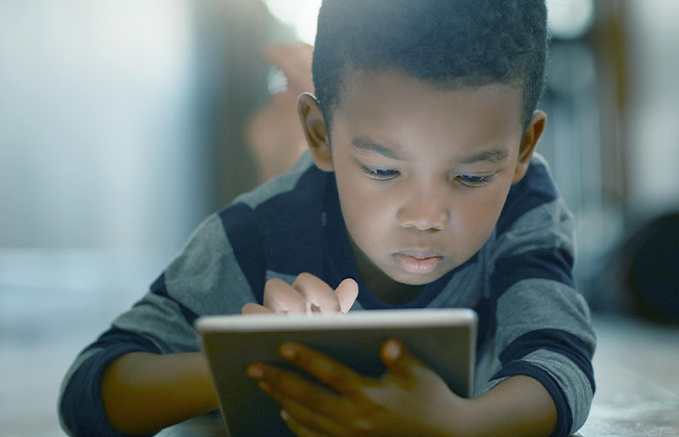 Young boy holding a tablet while laying stomach down