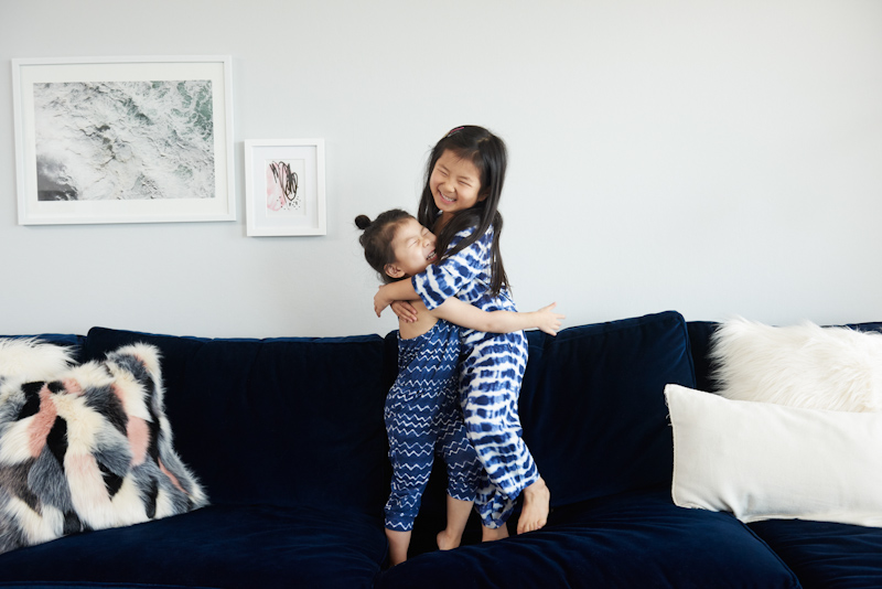 Two young girls hugging while standing on a couch.