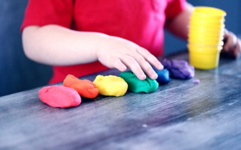 Child playing with six colours of play dough. Child's face is not in view.