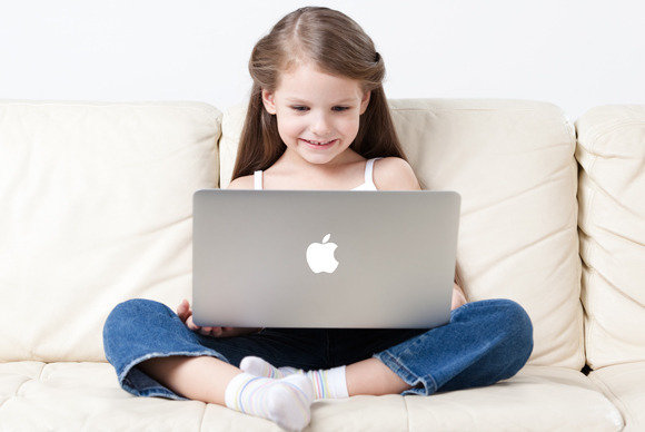 Young girl sitting on a couch looking at a laptop that is on her lap, she is smiling