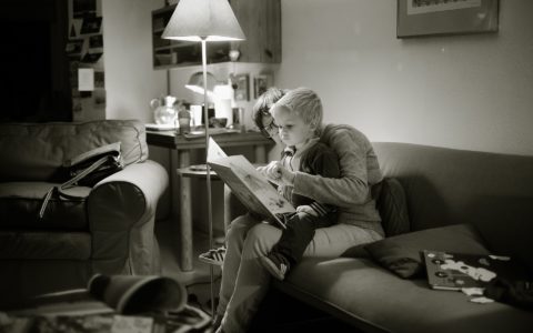 Black and white photo of a child and an adult reading a picture book together. Child is sitting in adult's lap.